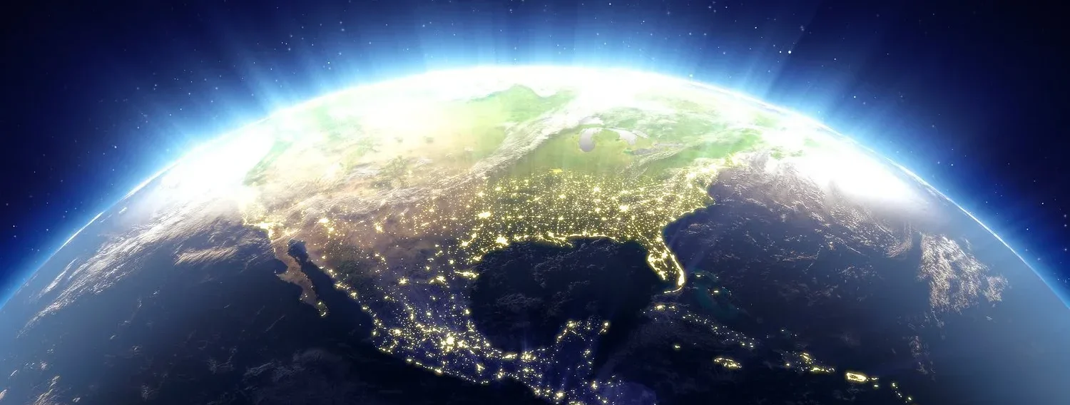 View of North America from space showing city lights across the continent, with the curvature of Earth and a glowing atmosphere visible against the dark background of space.