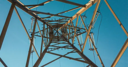 View looking up at the metal framework of an electrical transmission tower against a clear blue sky.