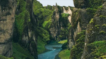 A narrow, winding river flows through a steep, moss-covered canyon with tall rock formations on both sides.