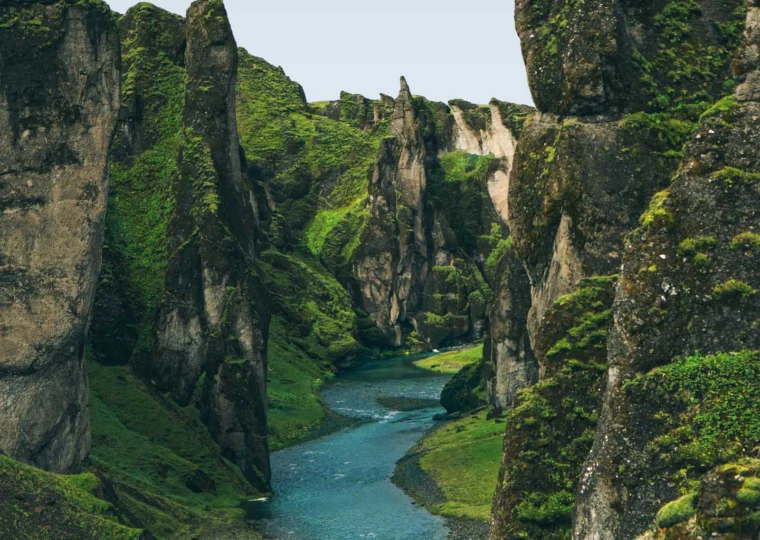 A narrow, winding river flows through a steep, moss-covered canyon with tall rock formations on both sides.
