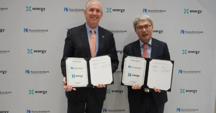 Two men in suits stand in front of a backdrop, holding signed documents from Korea Eximbank and X-energy, indicating a formal agreement or partnership.