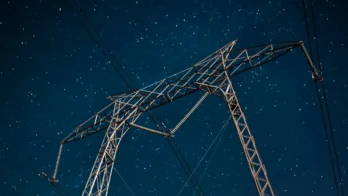 A tall metal electricity pylon with power lines set against a clear, starry night sky.