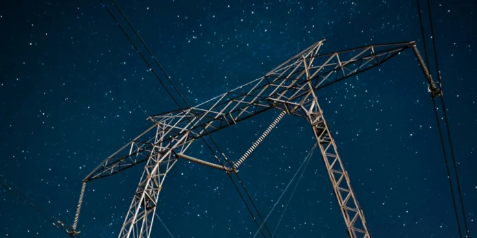 A tall metal electricity pylon with power lines set against a clear, starry night sky.