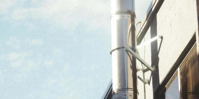 A metal ventilation pipe runs along the exterior wall of a building under a blue sky with scattered clouds.