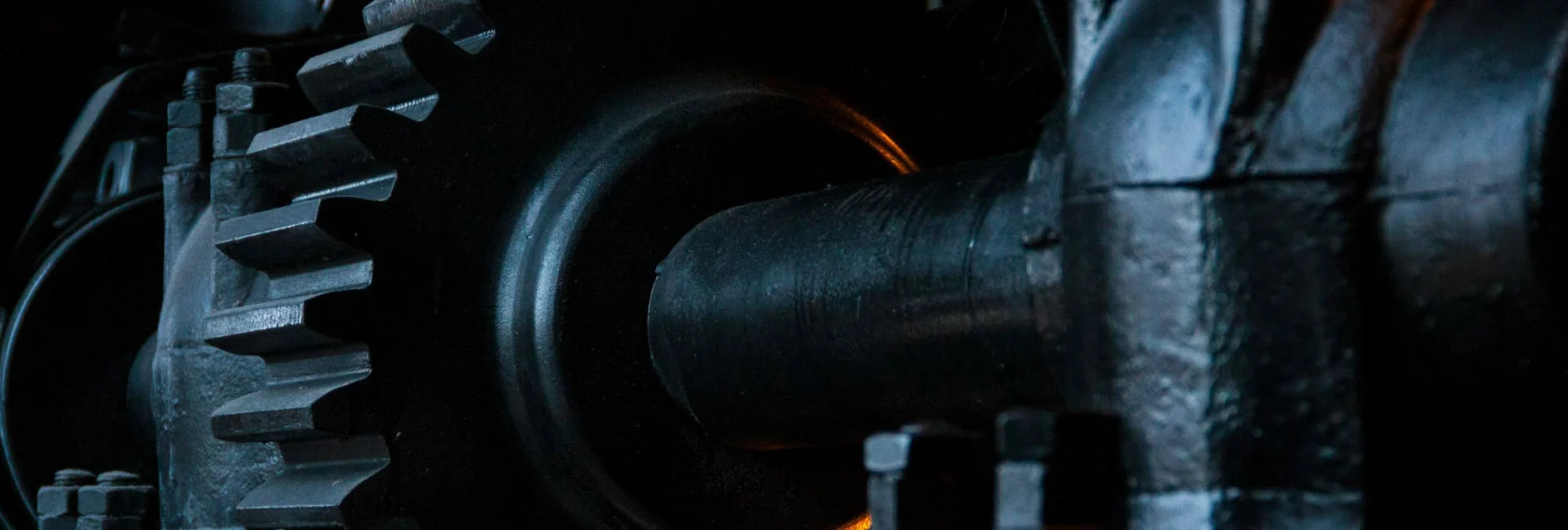 Close-up view of black metal gears and mechanical parts, showing industrial machinery components with detailed textures and low-key lighting.