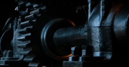 Close-up view of black metal gears and mechanical parts, showing industrial machinery components with detailed textures and low-key lighting.