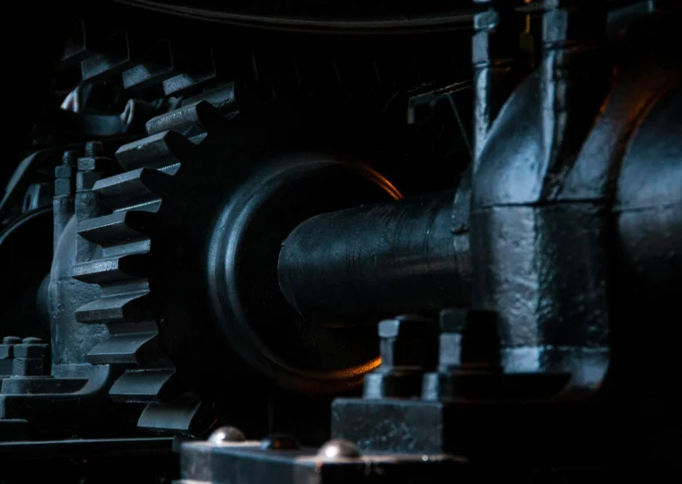 Close-up view of black metal gears and mechanical parts, showing industrial machinery components with detailed textures and low-key lighting.