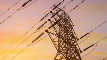 A metal electricity pylon with multiple power lines is silhouetted against a colorful sunset sky.