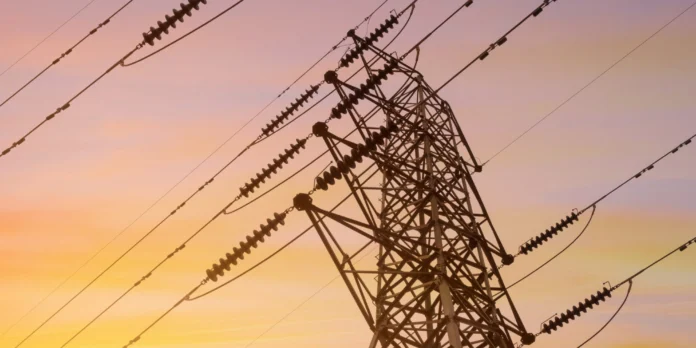 A metal electricity pylon with multiple power lines is silhouetted against a colorful sunset sky.