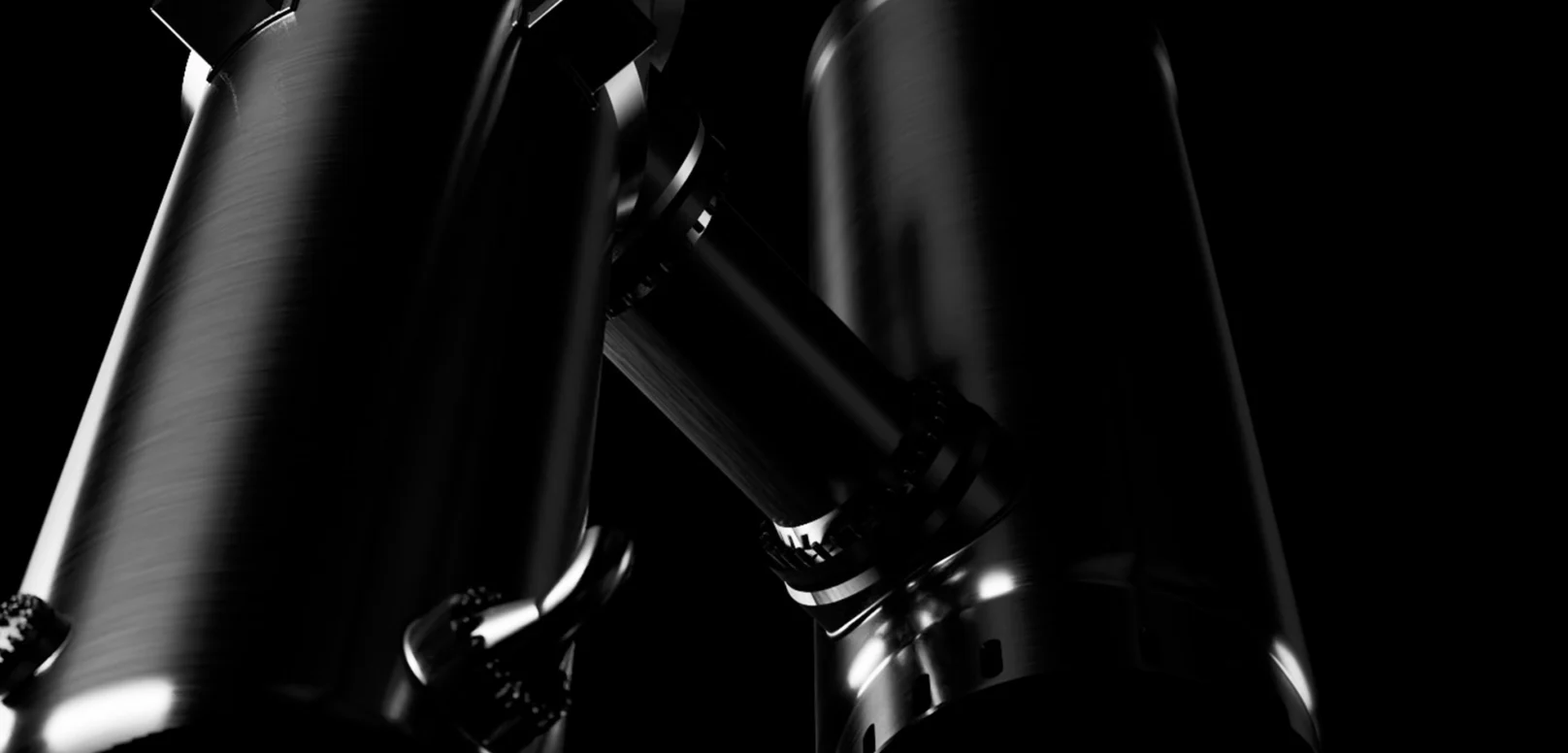 Two large metallic cylindrical objects joined by a connecting pipe, shown in dramatic lighting against a black background.