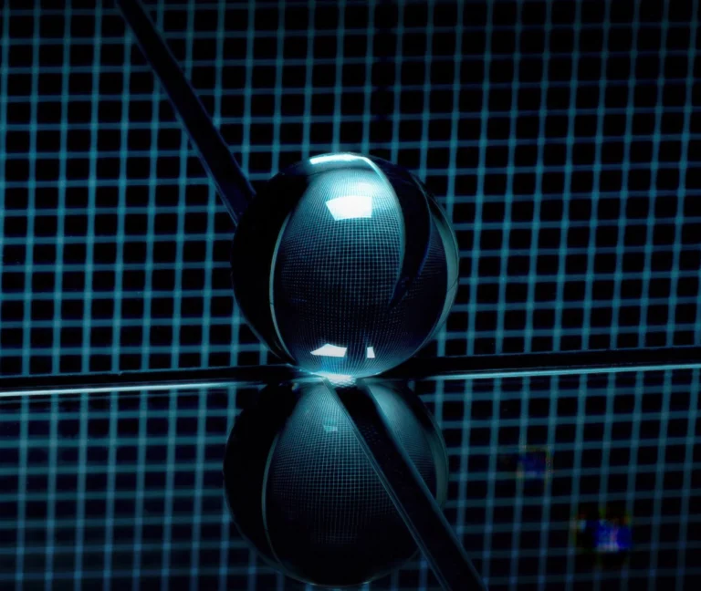 A glass sphere sits on a reflective surface with a blue grid pattern background, creating a symmetrical reflection beneath it.