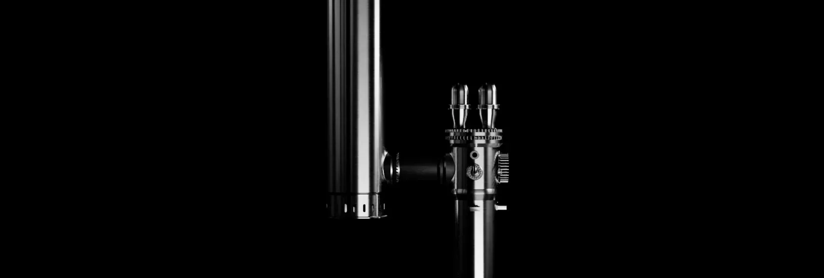 A metallic cylindrical object with various knobs and attachments against a solid black background.