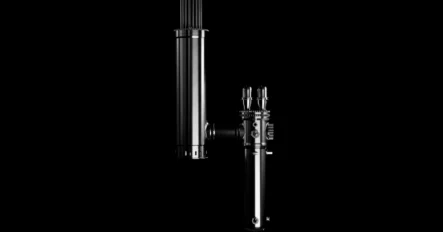 A metallic cylindrical object with various knobs and attachments against a solid black background.