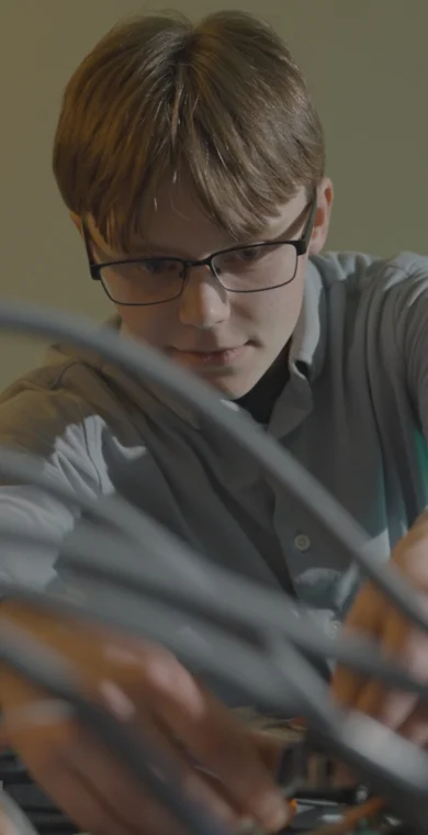 A person wearing glasses adjusts wires and equipment on a table, focusing intently on their work.
