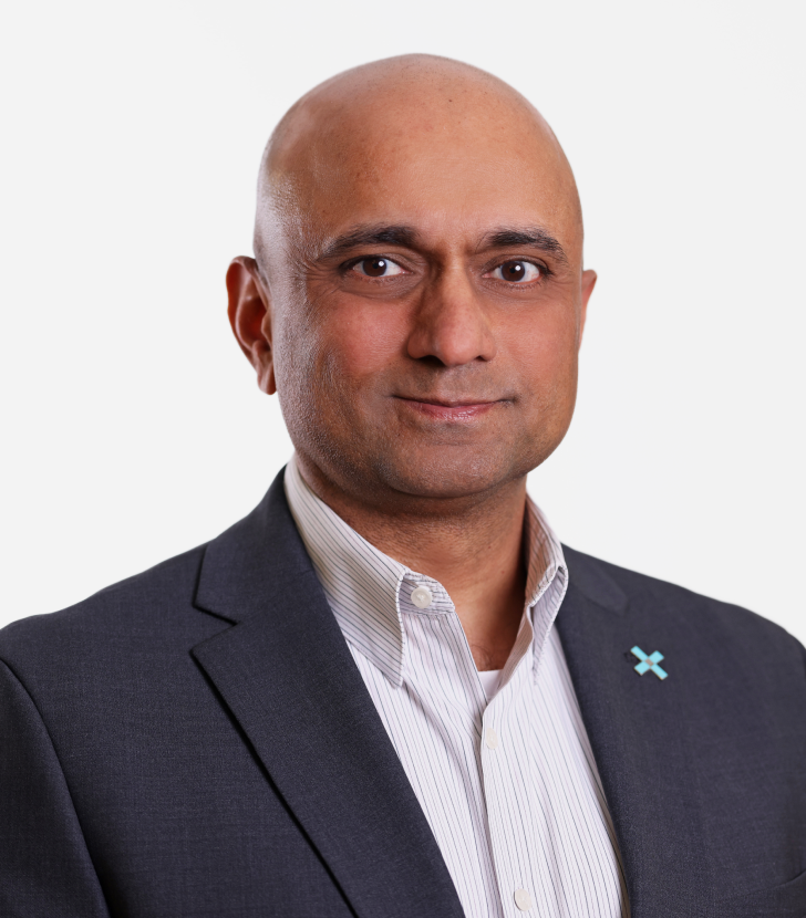 A man in a suit and striped shirt, wearing a small pin on his lapel, poses for a professional headshot against a plain white background.