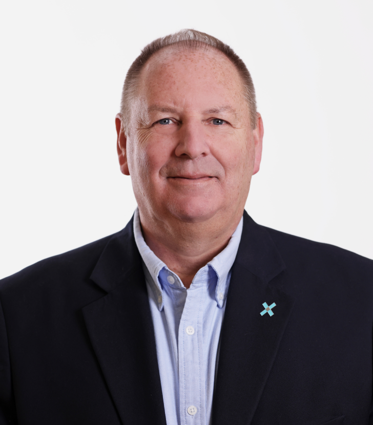 A middle-aged man wearing a dark blazer and light blue shirt, standing against a plain white background. He has short hair and is smiling slightly.