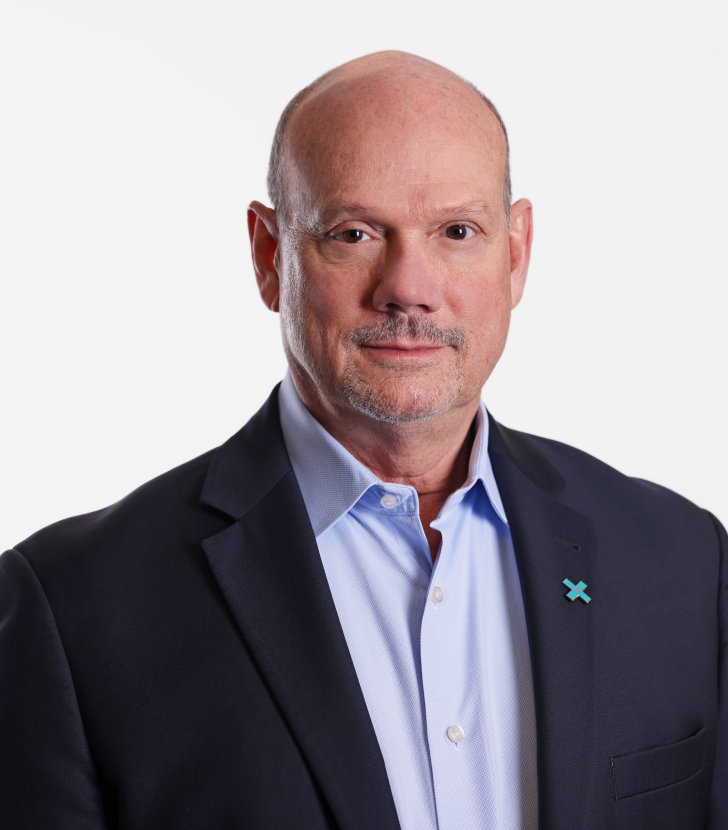 Bald man in a suit jacket and light blue shirt, standing against a plain white background, looking directly at the camera.
