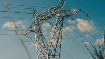 A metal electricity transmission tower with multiple power lines against a blue sky with scattered clouds.