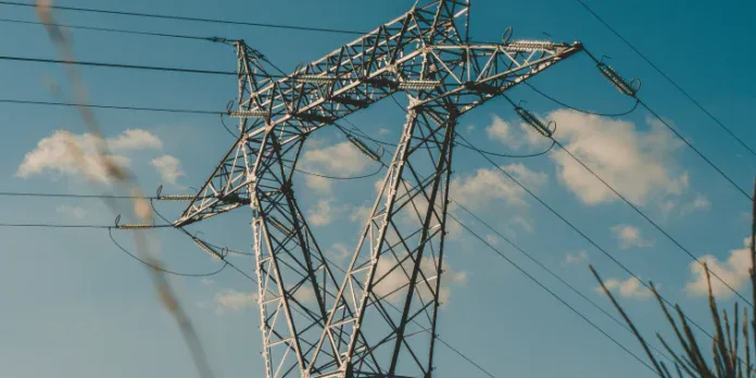 A metal electricity transmission tower with multiple power lines against a blue sky with scattered clouds.