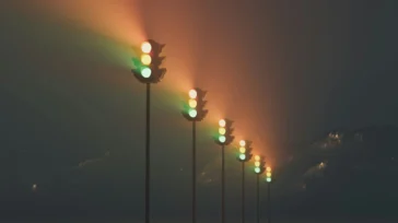 A row of traffic lights glowing green against a dark, mountainous landscape.