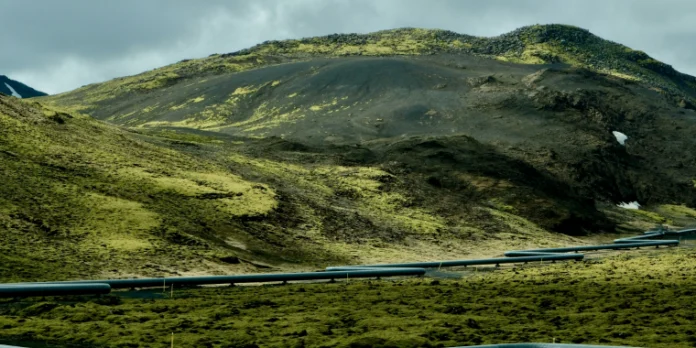 A long pipeline curves through a green, moss-covered volcanic landscape.